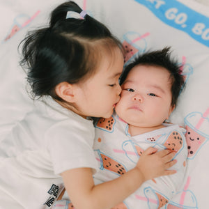 big sister kissing cute baby laying on boba milestone blanket by the wee bean